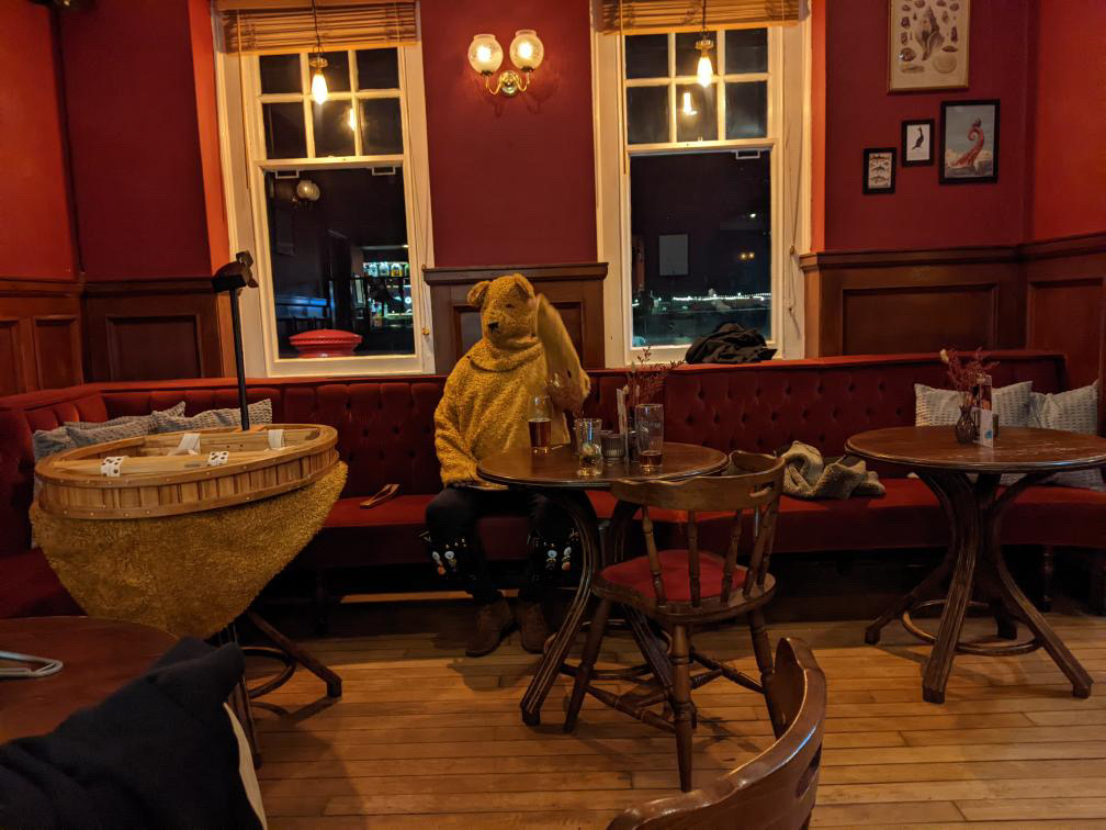 The Bear seated beside a table at the Mariner during Trad Folk Night