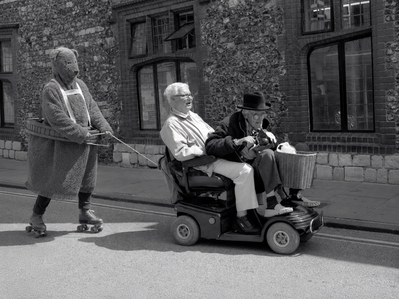 The Bear on roller skates being towed behind a mobility scooter