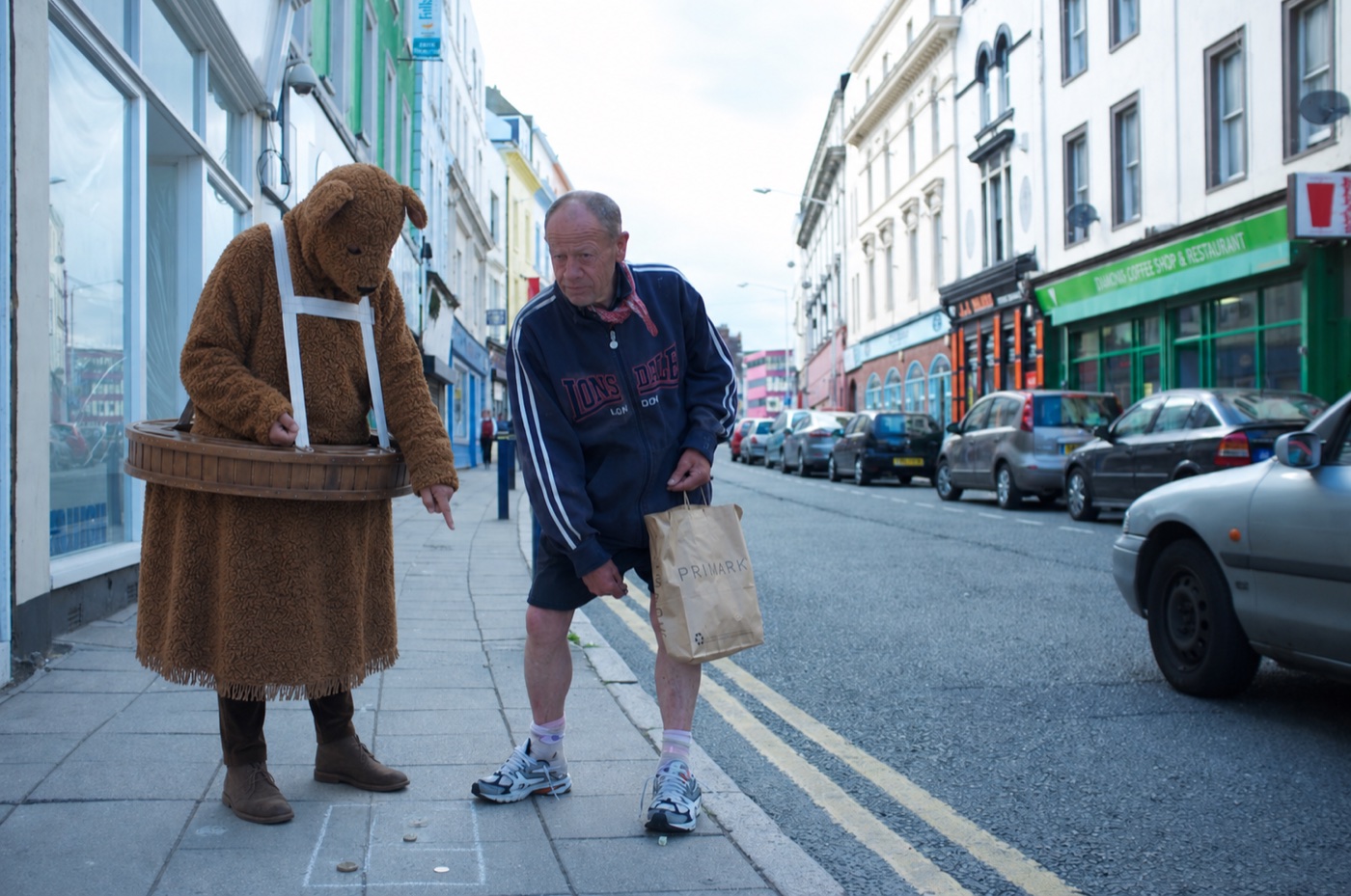 The Bear beside a man pointing at chalk squares and coins on a pavement
