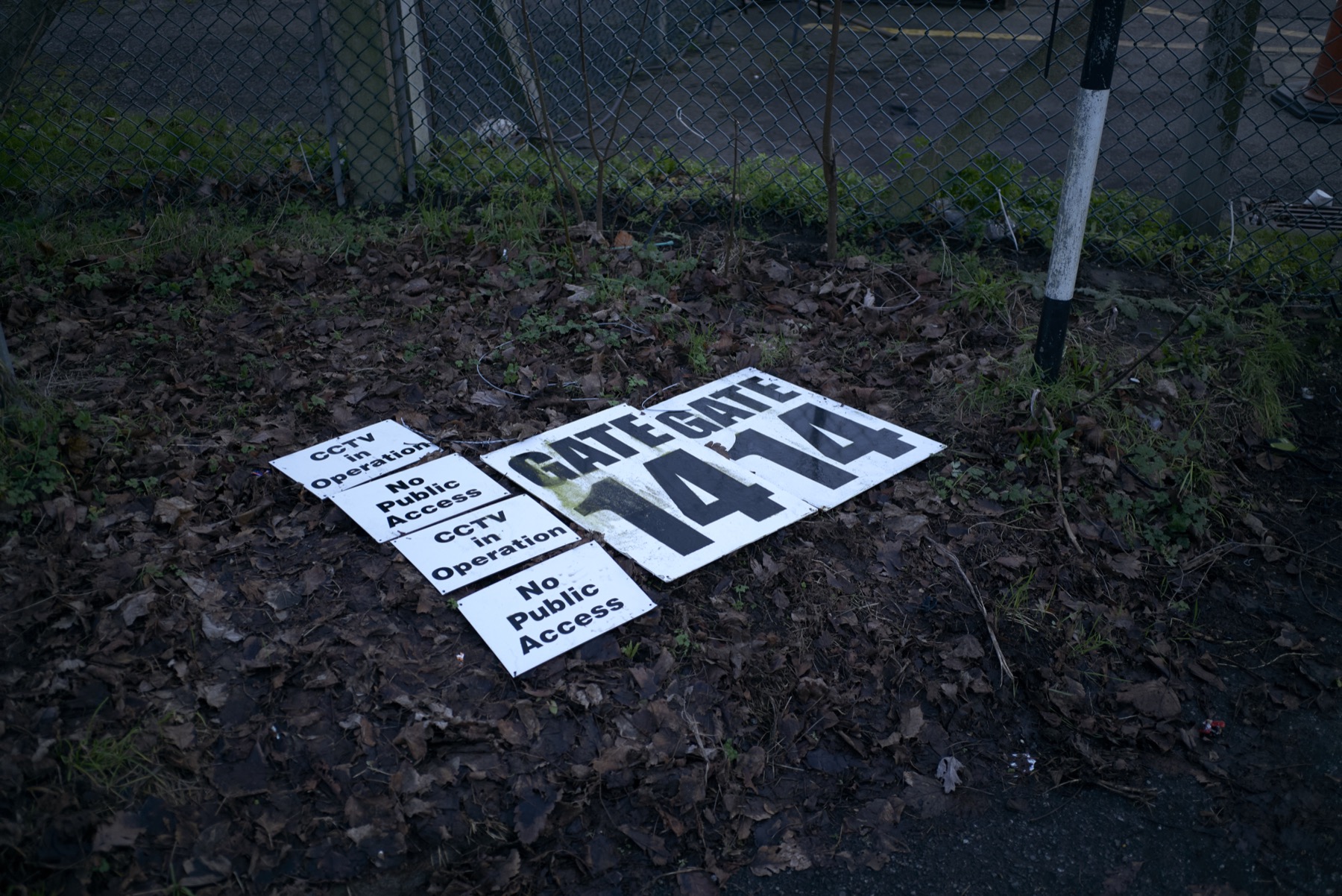 Discarded CCTV and no public access signs beside a chain-link fence