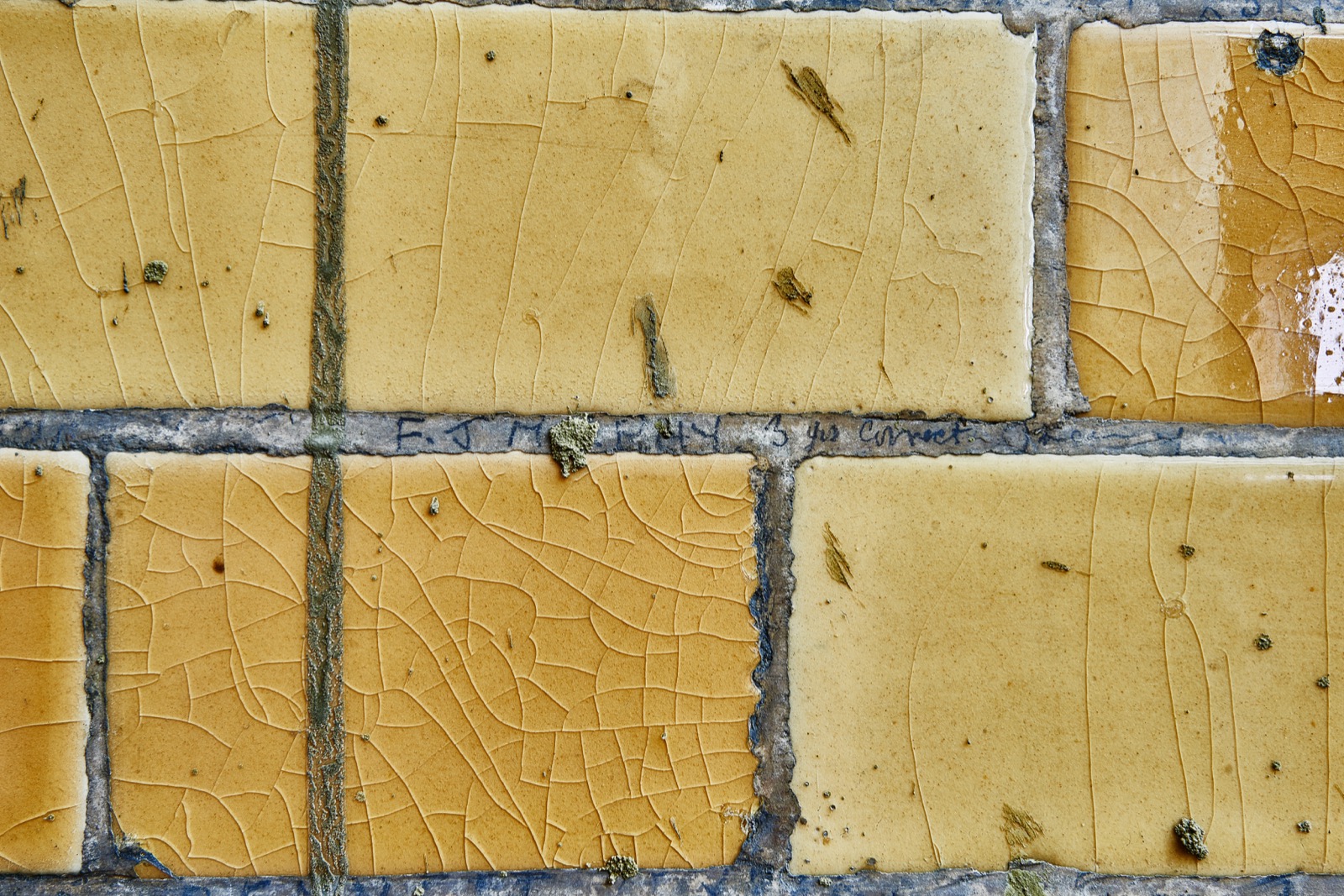Yellow tiled wall with faint pencil letters and surface damage